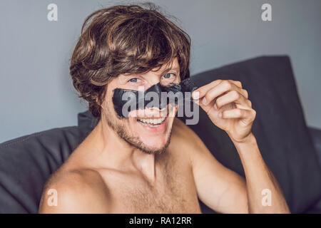 Glückliche Menschen mit schwarzer Maske auf dem Gesicht. Foto Mann empfangen von Wellnessanwendungen. Beauty Skin Care Concept Stockfoto