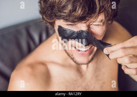 Glückliche Menschen mit schwarzer Maske auf dem Gesicht. Foto Mann empfangen von Wellnessanwendungen. Beauty Skin Care Concept Stockfoto