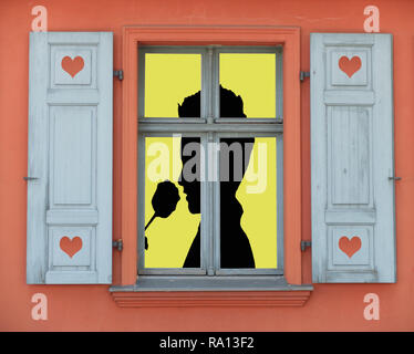 Valentines Tag Konzept, eine beleuchtete Fenster mit einer Silhouette eines romantischen Person riechende eine Rose Stockfoto