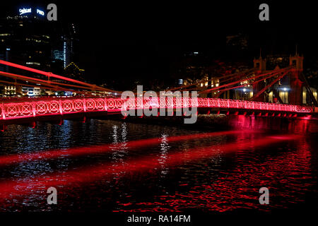 Die cavenaugh Brücke, die einzige Hängebrücke auf dem Singapore River, in Rot in der Nacht beleuchtet. Stockfoto