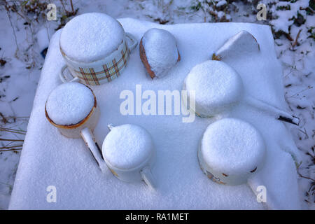 Gefrorene Alten rostigen Metall Aufläufe auf einem Tisch unter dem Schnee im Winter. Wie eine post-nuklearen Katastrophe. In der Nähe fotografiert im Winter Stockfoto