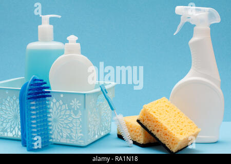 Plastikflaschen von Spülmittel, Glas- und fliesenreiniger im Korb, Schwämme, Bürsten und Pinsel auf blauem Hintergrund. Waschen und Reinigung Konzept. Stockfoto