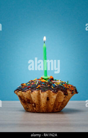 Lecker geburtstag Cupcake mit Schokoladenüberzug und Karamell, mit brennenden festliche Kerze auf blauem Hintergrund eingerichtet. Happy birthday minimalen Begriff. Stockfoto