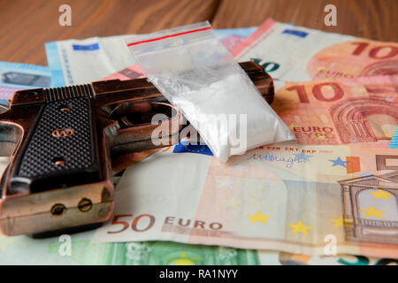 Schwarze Pistole und Pakete von Drogen vor dem Hintergrund der Euro auf einem Holztisch. Stockfoto