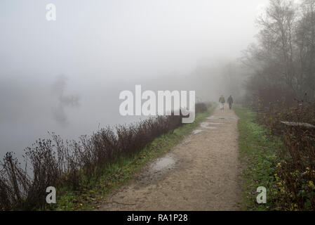 Zwei Männer zu Fuß neben dem See am Etherow Country Park an einem nebligen Winter morgen, Compstall, Stockport, England. Stockfoto