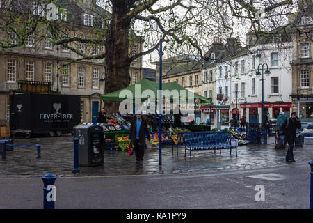 Eine Person mit einer Tragetasche zu Fuß entfernt von einem Obst und Gemüse Marktstand in Kingsmead Square in der Innenstadt von Bath Großbritannien auf einem nassen Winter morgen Stockfoto