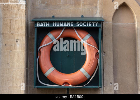 Eine orange Schwimmweste in einem offenen Holzhalter mit der Aufschrift "Badewanne humane Gesellschaft" an der Wand neben dem Kennet und Avon Kanal in Bath Somerset UK Stockfoto