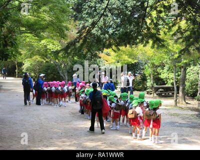 Gruppen von Jugendlichen der Schule werden die Kinder von der farbigen Kappen auf dem Kopf beim Besuch der Insel Miyajima identifiziert; sie alle tragen große Rucksäcke Stockfoto