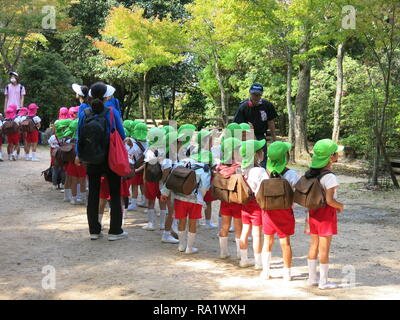 Gruppen von Jugendlichen der Schule werden die Kinder von der farbigen Kappen auf dem Kopf beim Besuch der Insel Miyajima identifiziert; sie alle tragen große Rucksäcke Stockfoto