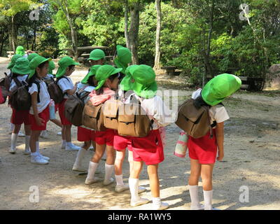 Gruppen von Jugendlichen der Schule werden die Kinder von der farbigen Kappen auf dem Kopf beim Besuch der Insel Miyajima identifiziert; sie alle tragen große Rucksäcke Stockfoto