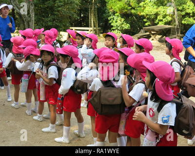 Gruppen von Jugendlichen der Schule werden die Kinder von der farbigen Kappen auf dem Kopf beim Besuch der Insel Miyajima identifiziert; sie alle tragen große Rucksäcke Stockfoto