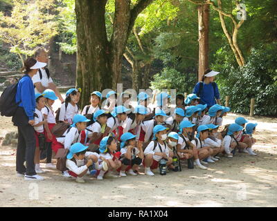 Gruppen von Jugendlichen der Schule werden die Kinder von der farbigen Kappen auf dem Kopf beim Besuch der Insel Miyajima identifiziert; sie alle tragen große Rucksäcke Stockfoto