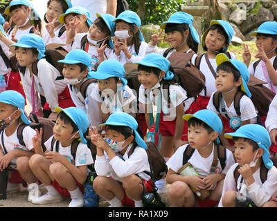 Gruppen von Jugendlichen der Schule werden die Kinder von der farbigen Kappen auf dem Kopf beim Besuch der Insel Miyajima identifiziert; sie alle tragen große Rucksäcke Stockfoto