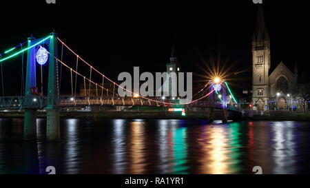 Schöne vor Weihnachten abends zu Fuß in Inverness, Schottland. Schöne Weihnachten Lichter und Riverside am Fluss Ness. Alte Kirche im Hintergrund Stockfoto