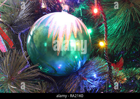 Eine enge Sicht auf eine grüne Blätter Weihnachtsbaum mit elektrischer Beleuchtung Dekoration, hängende Ornamente und eine große Christbaumkugel in einer hellen Atmosphäre. Stockfoto