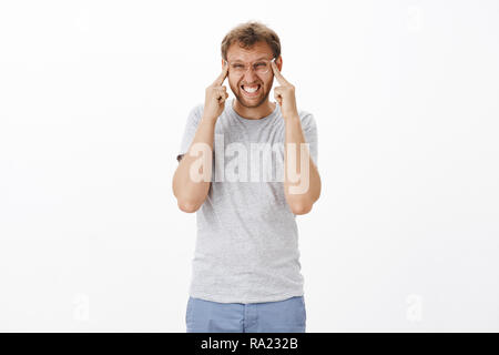 Verwirrt intensive männlichen Erwachsenen mit Borsten in Gläsern Aufeinanderpressen der Zähne schielen und Stretching Augenlider zu sehen offenbar Probleme mit den Augen, während neue Brillen, Optiker Store über weiße Wand Stockfoto