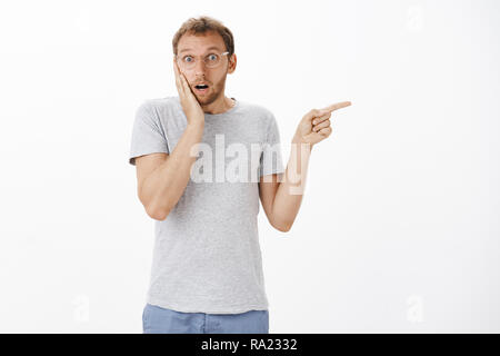 Kerl sprechen mit Nachbarn lernen Schockierende Neuigkeiten. Portrait von betäubt cute besorgt Europäische Männlich in Gläsern holding Palm auf der Wange von Empathie und schüttelte nach rechts mit Zeigefinger Stockfoto