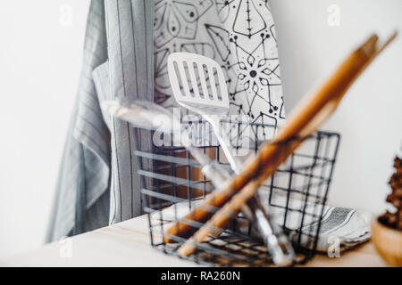 Küche Silber und Holz- Utensilien auf dem Tisch und Schürzen an der Wand. Stockfoto