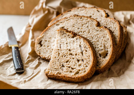 Handwerker in Scheiben geschnittene Hausgemachte Sauerteigbrot Schichten mit Papiertüte/Paket oder Craft-Papier. Bio Bäckerei Essen. Stockfoto