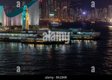 Die Tsim Sha Tsui Star Ferry Piers bei Nacht mit Blick auf den Uhrturm und kulturelles Zentrum, und über die Causeway Bay auf Hong Kong Island Stockfoto