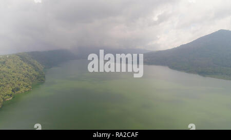 Lake Buyan Ufer mit tropischer Vegetation an bewölkten Tag abgedeckt. Berg mit Pisten überdachte tropische Vegetation. Bali Landschaft, See zwischen Bergen, Himmel, Wolken. Stockfoto