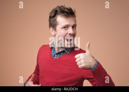 Gerne schöner Mann im roten Pullover mit Daumen hoch Stockfoto