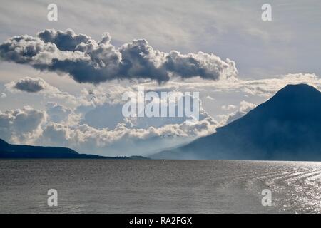 Ein kleines Boot Umsatzmechanismen übersteigt die Versammlung Sturmwolken in zwischen zwei Vulkanen an einem See. Stockfoto