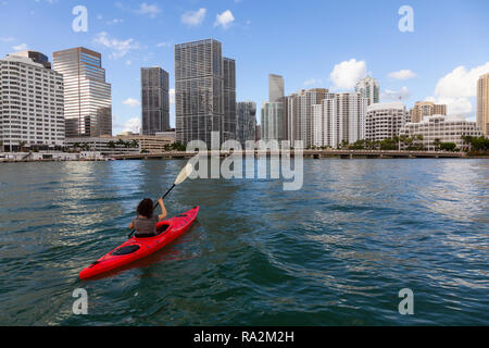 Abenteuerliche Mädchen Kajak vor einem modernen Stadtzentrum Stadtbild während eines sonnigen Abend. In Miami, Florida, Vereinigte Staaten von Amerika übernommen. Stockfoto