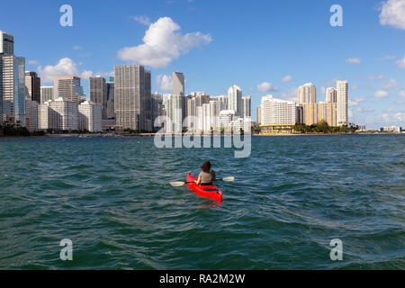 Abenteuerliche Mädchen Kajak vor einem modernen Stadtzentrum Stadtbild während eines sonnigen Abend. In Miami, Florida, Vereinigte Staaten von Amerika übernommen. Stockfoto