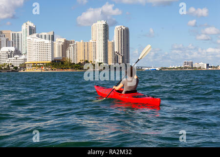 Abenteuerliche Mädchen Kajak vor einem modernen Stadtzentrum Stadtbild während eines sonnigen Abend. In Miami, Florida, Vereinigte Staaten von Amerika übernommen. Stockfoto