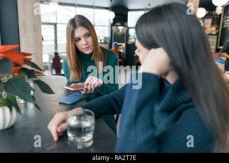 Sprechen junge Frauen, Mädchen im Winter cafe lächelnd und sprechen, Sitzen, trinken sauberes Wasser in Glas und über Handy, rot Weihnachtsstern Weihnachten Stockfoto