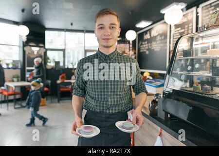 Junge lächelnde Menschen arbeiten im Coffee Shop holdng zwei Platten mit Makronen. Stockfoto