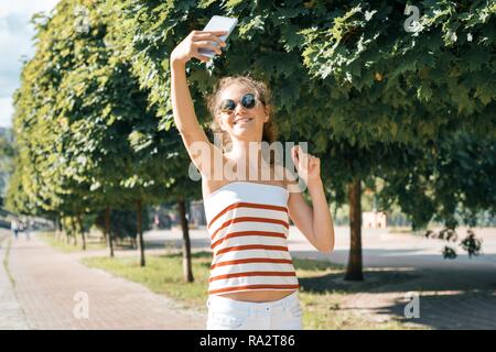 Junge Mädchen blogger nimmt Fotos und Videos für sein Blog. Mädchen lächelnd auf der Straße von den Sommer City Park. Stockfoto