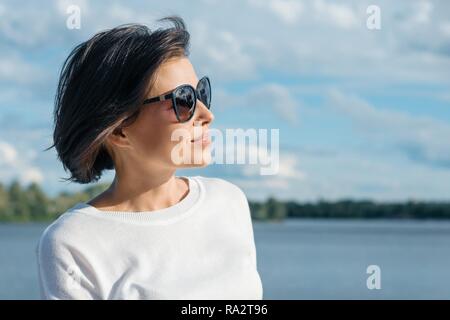 Portrait von reife Frau im Profil bei Sonnenbrillen auf die Natur in der Nähe des Flusses. Stockfoto