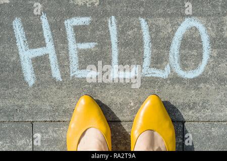 Weibliche Füße mit Text hallo auf Asphalt geschrieben. Stockfoto