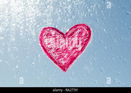 Rotes Herz mit Lippenstift auf dem Fenster mit Wassertropfen gemalt. Hintergrund blau sonnigen Himmel, Tropfen glänzen in der Sonne. Stockfoto