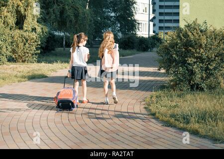 Ansicht der Rückseite zwei Schulmädchen Freundinnen Grundschüler gehen mit Schultasche auf dem Hof. Stockfoto