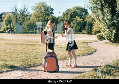 Ansicht der Rückseite zwei Schulmädchen Freundinnen mit Rucksäcken Eis essen. Stockfoto