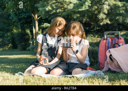 Zwei kleine Schulmädchen mit einem Smartphone. Kinder spielen, Lesen, am Telefon, im Park, goldenen Stunde. Menschen, Kinder, Technik, fr Stockfoto