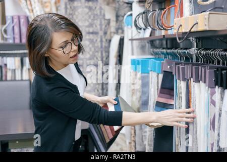 Stoffe lagern, erwachsene Frau suchen und berührt, Proben, weibliche Designer wählt Stoffen für die Inneneinrichtung. Stockfoto