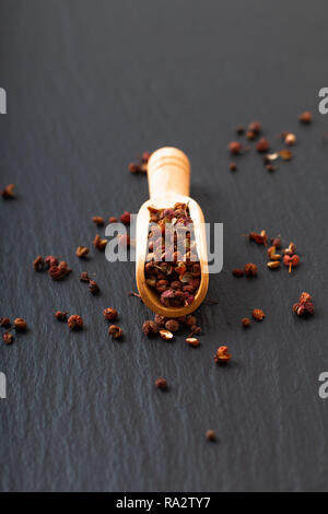 Chinesischer Pfeffer, Sichuan Pfeffer in Holz- Schaufel auf schwarzem Schiefer Stein Platte mit Kopie Raum Stockfoto