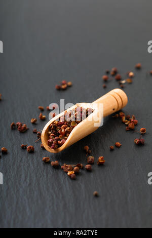 Chinesischer Pfeffer, Sichuan Pfeffer in Holz- Schaufel auf schwarzem Schiefer Stein Platte mit Kopie Raum Stockfoto