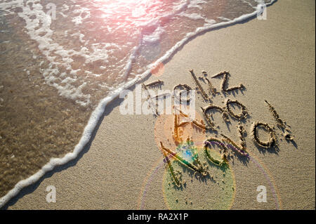 Portugiesische Feliz Ano Novo (Frohes Neues Jahr) Nachricht handschriftlich in strukturierte Schriftzug auf glatten Sand mit einem frischen neuen Welle an einem brasilianischen Strand Stockfoto