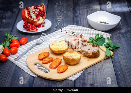 Auf dem Board sind zwei Scheiben gebackenes Fleisch, zwei Scheiben und gebackene Kartoffeln Karotten Scheiben, einem karierten Serviette von Flachs, in eine Schüssel sind multi-col Stockfoto