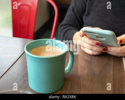Frau mit Handy während des Wartens auf eine heiße Schokolade in Teal Schale abkühlen lassen Stockfoto