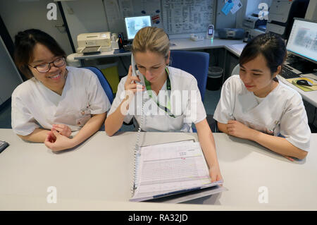 Rostock, Deutschland. 21 Dez, 2018. Anh Tu Tun (l) und Thi als Huyen Nguyen (r), Vietnamesisch Krankenschwestern in der Ausbildung, den Dienstplan in der Onkologie mit Janine Schreiber, Leiter Krankenschwester und der Gesundheit der Arbeitnehmer diskutieren. 16 Frauen und 4 Männer aus Vietnam begann die Ausbildung in der Krankenpflege in der universitären Medizin an der Ende August 2018. Wie erwartet, der Umgang mit der Deutschen Sprache ist immer noch schwierig, aber von der technischen Seite gibt es keine Probleme. Quelle: Bernd Wüstneck/dpa/Alamy leben Nachrichten Stockfoto