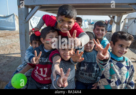 19. Dezember 2018 Irak, Hasan Sham: Kinder beobachten, den Besuch von Außenminister Maas zu den Hasan Sham Flüchtlingslager und den Sieg Zeichen zeigen. Das Zeltlager in der Nähe der weitgehend zerstörten ehemaligen ist Hochburg von Mossul bietet Platz für 3.300 der 1,8 Millionen intern Vertriebene im Irak. Foto: Jens Büttner/dpa-Zentralbild/ZB Stockfoto