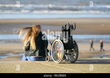 Behinderte Frau mit Gehhilfe in Blackpool, Lancashire. Januar 2019. Wetter in Großbritannien. An einem kalten, stürmischen, aber sonnigen Tag an der Strandpromenade und am Vorgewende. Urlauber, die die Stadt zu Neujahr besuchen, können sich am Strand und am Vorland dieses britischen Badeorts leicht bewegen. Quelle: MediaWorldImages/AlamyLiveNews Stockfoto