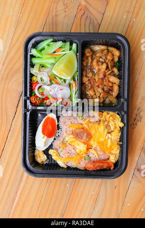 Gebratener Reis mit Garnelen paste gehören Mango, Eier, Schweinefleisch, Zwiebeln, Gemüse in Box schwarz/Thai Essen auf einem Holz Tisch Hintergrund Stockfoto