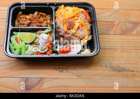 Gebratener Reis mit Garnelen paste gehören Mango, Eier, Schweinefleisch, Zwiebeln, Gemüse in Box schwarz/Thai Essen auf einem Holz Tisch Hintergrund Stockfoto